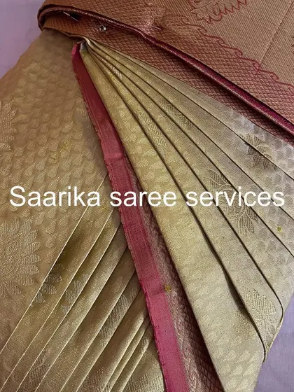 A soft gold saree with a pink border, pleated for a graceful and elegant fall.