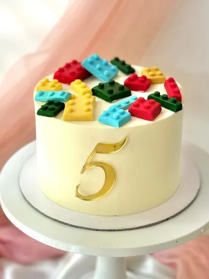 A simple yet effective Lego-themed cake. The clean white buttercream is the perfect base for the colourful fondant Lego bricks and a golden number '5'.