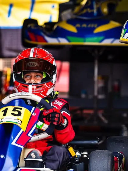 A young driver in his red race suit, looking focused in his kart.