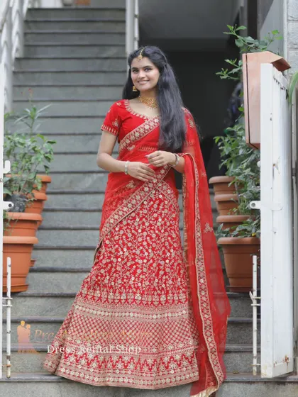 The red and gold lehenga is shown on a staircase, highlighting its elegant drape and flow.