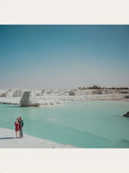 A wide shot of a couple standing by a turquoise lake in a surreal white landscape. This location provides a unique and unforgettable backdrop for pre-wedding photos.