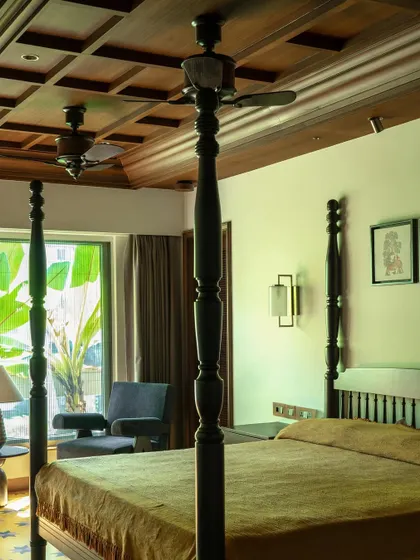 The master bedroom, featuring a classic four-poster bed and a coffered wooden ceiling. The design creates a sanctuary that is both grand and intimate, rooted in a timeless Indian aesthetic.