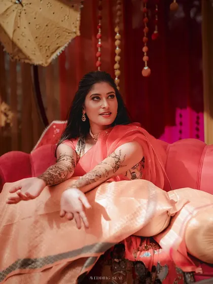 The bride in a moment of quiet contemplation, bathed in warm, natural light. Her iridescent saree and serene expression create a portrait of pure elegance.
