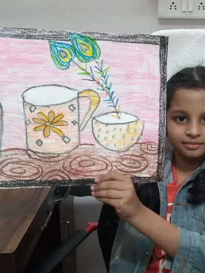 Neev, a 2nd standard student, with his still life drawing. He has used oil pastels to draw a collection of cups and a vase with peacock feathers.