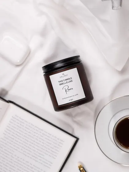 A cozy, "morning in bed" flat lay featuring a Delight Candle. The styling with a book, coffee, and AirPods creates a relatable, relaxing lifestyle scene.