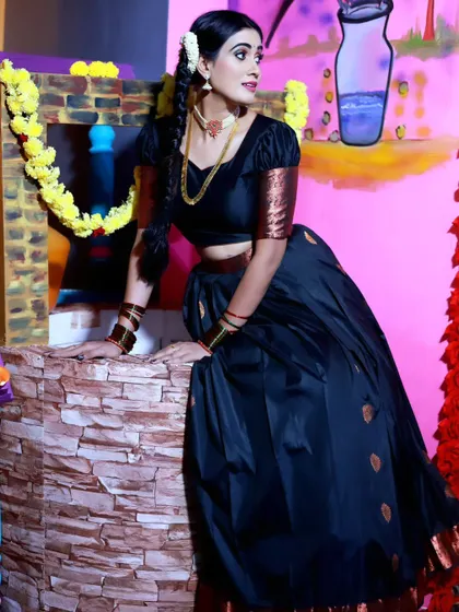 A model posing in a traditional black half-saree, showcasing the outfit's elegance against a vibrant, painted backdrop.