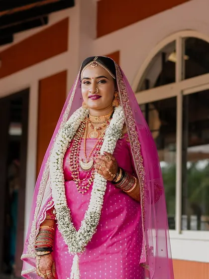 A full-length portrait of a Coorgi bride in a vibrant pink saree for her muhurtham. Her makeup is classic and beautiful.
