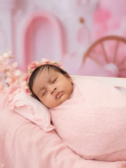 A close-up of this sweet baby girl, sleeping peacefully on a miniature bed with a pink floral crown. The background features a magical castle for a true fairytale feel.