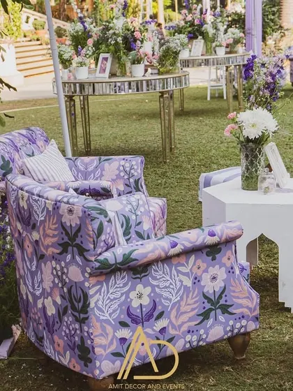 A cozy and picturesque seating nook in a garden setting, featuring a floral-printed armchair and other custom furniture in shades of purple.