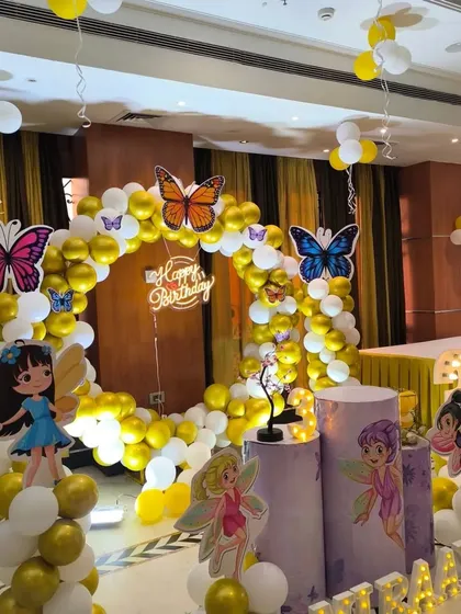 A beautiful fairy and butterfly themed party setup. This decoration uses a gold and white balloon ring arch, accented with large, colorful butterflies and fairy cutouts.