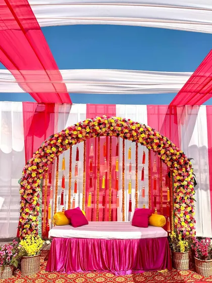 We love working with bright, happy colors for Mehendi and Haldi ceremonies. This vibrant setup features a full floral arch and a backdrop of colorful tassels under a pink and white tent, creating the perfect festive 'shaadi wala ghar' feel.