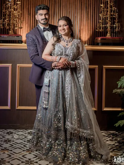 A classic couple portrait from their reception. The bride looks stunning in a grey embellished lehenga, with full glam makeup and a modern hairstyle, perfectly complementing the groom's sharp suit.