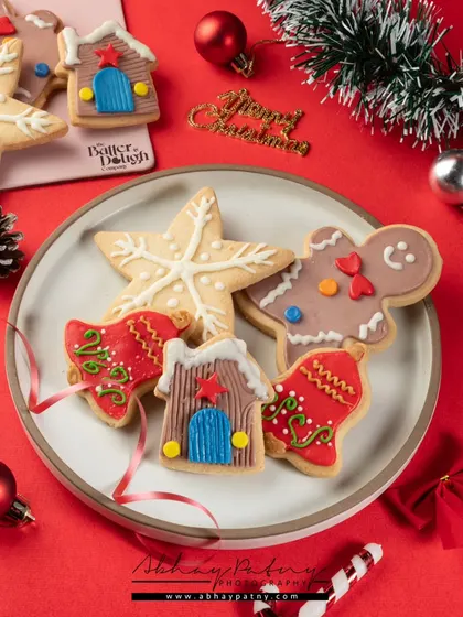 These Christmas-themed cookies are arranged playfully on a plate to showcase their fun shapes and detailed icing. The red background and festive props complete the holiday mood.