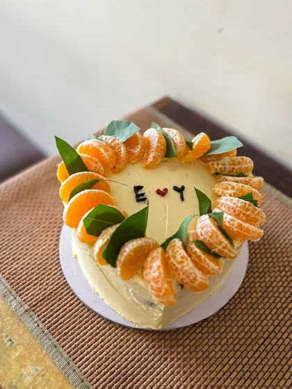 A rustic and minimal heart-shaped cake. It's decorated with a crown of fresh mandarin orange slices and leaves, with simple initials in the center for a personal touch.