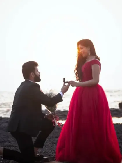 A beach proposal scene. Our classic red off shoulder gown is the perfect rental for capturing this milestone moment.