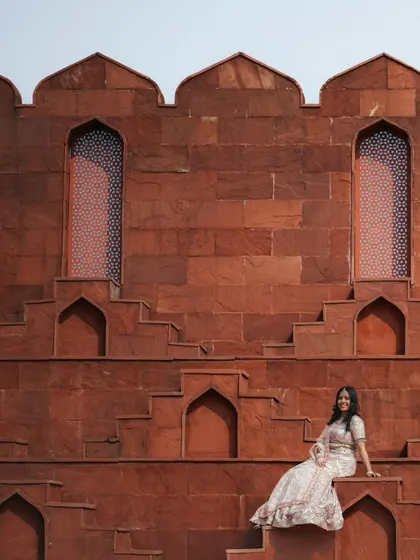 A stunning solo portrait of the bride seated against the unique geometric patterns of a red sandstone step-well wall, highlighting her elegant lehenga.