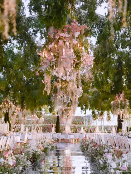 A magical reception setting in a romantic garden, with a mirrored walkway reflecting the floral chandeliers hanging from the trees. The design was captivating and truly immersive.