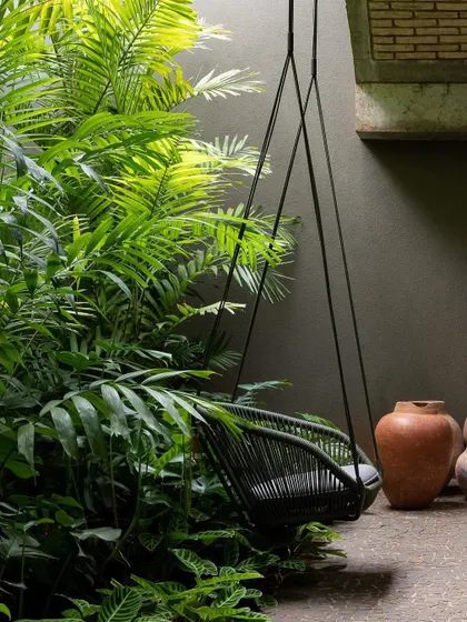 This tranquil corner features a hanging chair surrounded by lush greenery. The addition of terracotta pots on the side adds a rustic touch to the modern relaxation spot.