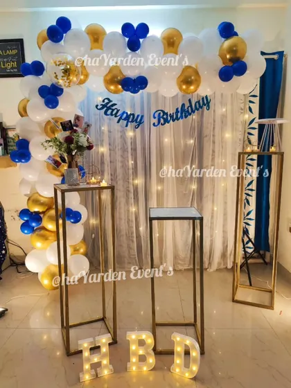 A simple balloon arch in blue, white, and gold against a curtain with fairy lights. This is a classic and elegant choice for a home birthday party.