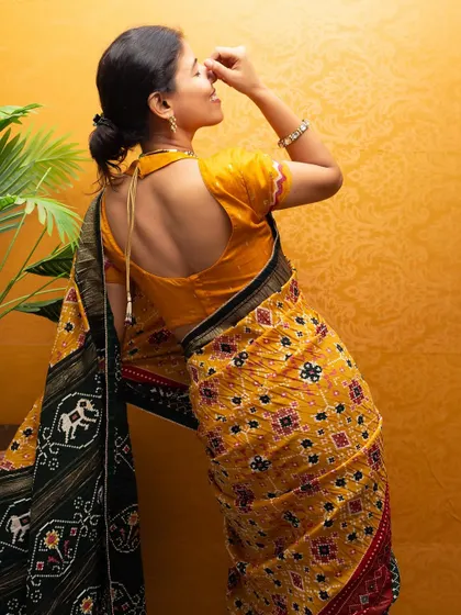 This back-profile pose highlights the intricate blouse design and the beautiful border of the Patola saree.