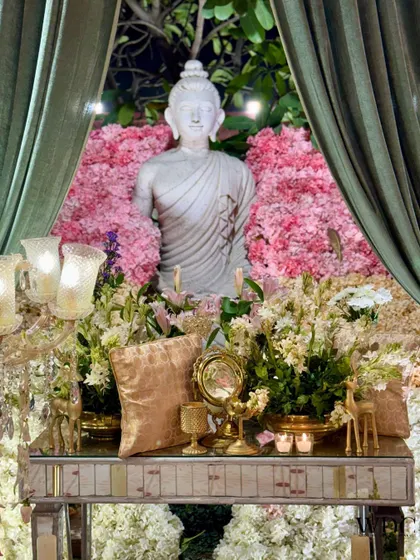 A close-up of the calming Buddha installation, surrounded by a bed of pink and white flowers and elegant golden decor pieces.