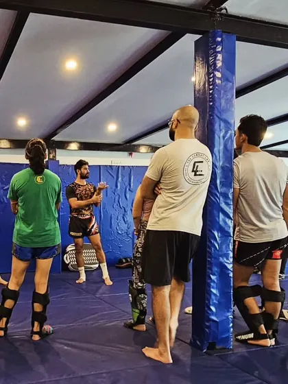 Students listening as the coach details the finer points of a technique. Everyone is geared up in shin guards, ready to drill what they've just learned.