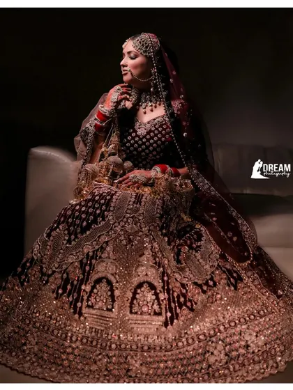 A full-length shot of a bride seated, her magnificent and heavily embroidered lehenga spread out in all its glory.