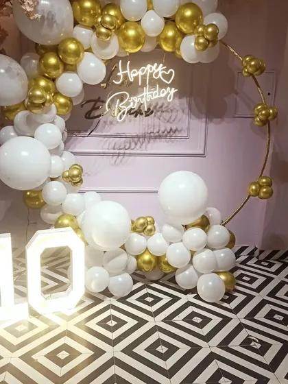 Here is a simple yet very classy ring decoration for a 10th birthday party at home. The white and gold chrome balloons, paired with a neon sign and light-up numbers, create a sophisticated look for a milestone celebration.
