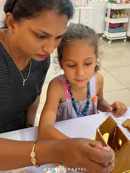 An instructor helps a young girl get started on her gingerbread house, showing her how to apply the icing.