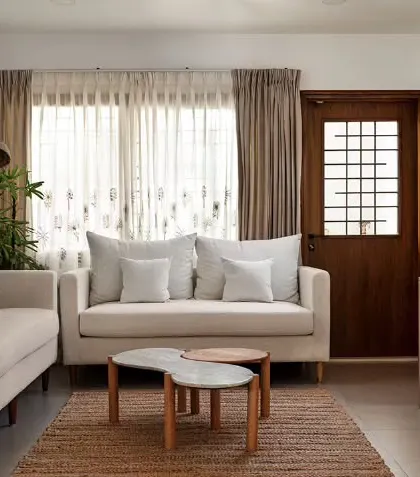 The formal living space, designed with a neutral and earthy palette. An organically shaped marble and wood table sits on a jute rug, complemented by off-white sofas and a sleek rattan console.