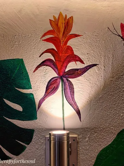 The uplighting on the wall highlights a tropical flower and butterfly, adding drama and drawing attention to the smaller, delicate details of the balcony mural.