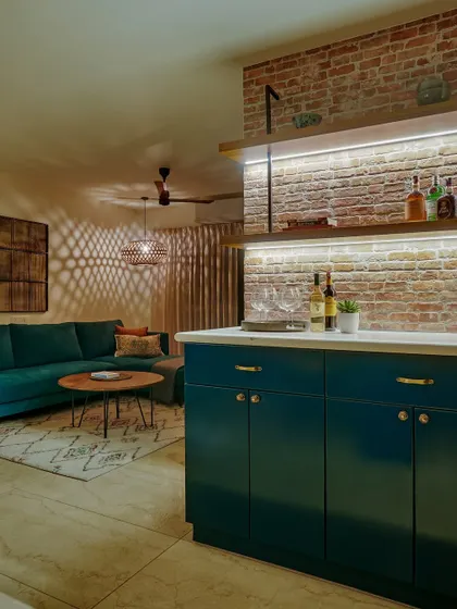 A moody bar area with an exposed brick wall and a deep teal cabinet. The under-shelf lighting creates a warm and inviting ambiance, perfect for a gloomy Bangalore day.