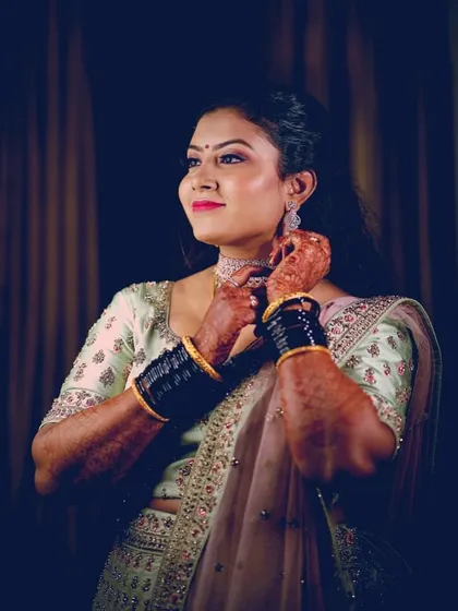 A bride getting ready for her reception. This candid shot shows her adjusting her necklace, giving a glimpse of her elegant lehenga and the soft glam makeup.