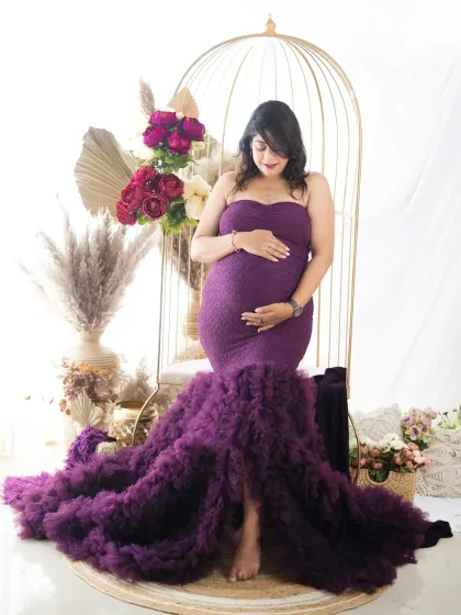 A beautiful mom-to-be posing in a purple ruffled gown. The barefoot, grounded pose adds a touch of natural elegance to this studio shot.