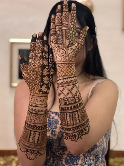 A bride peeking through her henna-adorned hands, a classic pose that highlights the beautiful back-of-hand design.