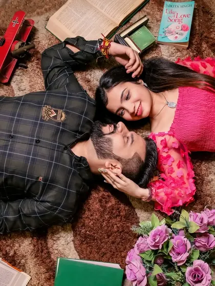 An intimate shot of a couple lying on a rug, surrounded by books and flowers, lost in each other's eyes.