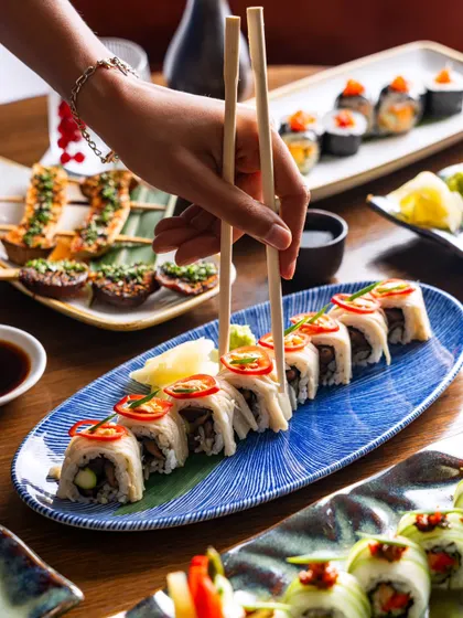 A lifestyle shot showing chopsticks picking up a piece of sushi from a platter. This action-oriented image is highly effective for social media content.