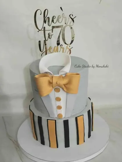 Cheers to 70 years! This two-tier tuxedo-style cake is a dapper and distinguished choice for a milestone birthday, complete with a bow tie and a "Cheers to 70 Years" topper.