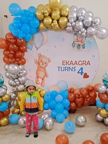 A cute teddy bear theme for a 4th birthday, with a child posing in front of the colorful balloon setup.