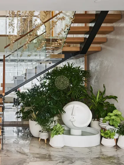 A serene water fountain from Claymen sits at the base of the staircase, surrounded by plants. This feature brings a sense of calm and a connection to nature right into the heart of the home.