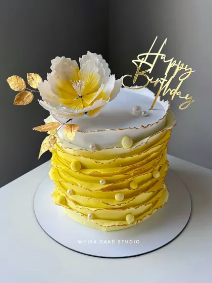 A classic ruffle cake in a sunny yellow hue. This fondant-covered cake is topped with a large, handcrafted white and yellow sugar flower.