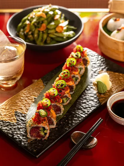 A platter of spicy tuna rolls garnished with jalapeños. The composition includes a drink and other dishes to create a complete dining scene.