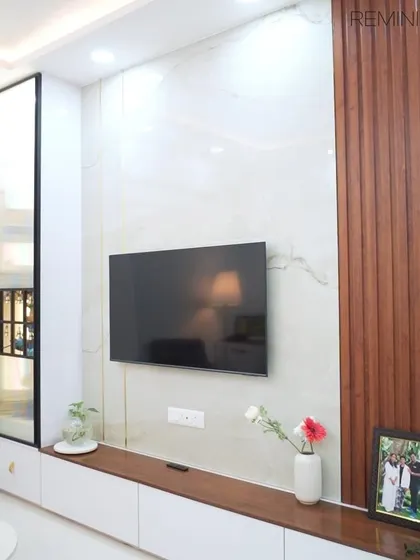 This TV unit combines a marble-finish back panel with vertical wooden louvers and a sleek white console. A tall glass display cabinet provides an elegant space for showcasing decor.