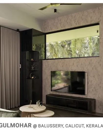 The TV and lounge area in Gulmohar, where minimalist furniture and textured walls are complemented by reflections of the garden in the large windows.