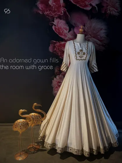 Step into a world of elegance with this floor-length white Anarkali-style gown, a canvas of artistry embellished with meticulous hand embroidery and opulent gold embellishments.