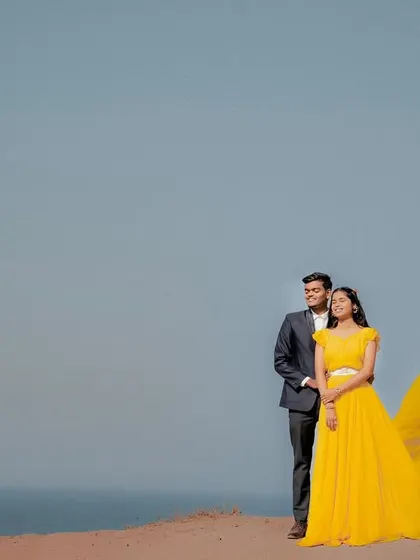 A wide shot showcasing the beauty of the coast. The couple's outfits, especially her yellow trail gown, add a beautiful focal point to the landscape.