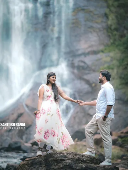 A romantic pose with the couple holding hands, set against the soft, misty spray of a waterfall.