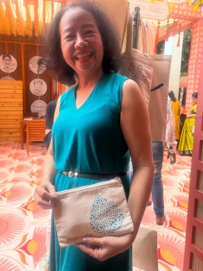 The joy is contagious. A smiling guest shows off her finished pouch, printed with a beautiful traditional motif and the couple's custom wedding hashtag. It's a keepsake she can use for years to come.