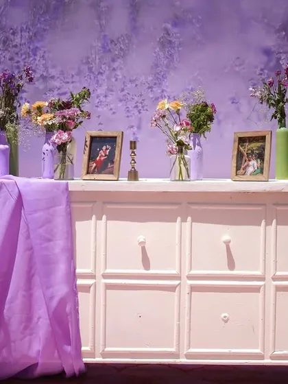 A personalized memory station. We used a white console table to display the couple's photos, surrounded by flowers in pastel-painted bottles and woven baskets, creating a heartfelt and stylish corner.