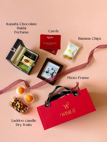 A flat lay of the contents of our red Rakhi hamper. It includes a watch box, Kunafa chocolate, perfume, a resin Rakhi, a photo frame, and more.
